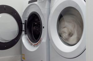 Front-loading household clothes dryer with clothes tumbling in motion blur on a high-heat cycle inside a clean home laundry room, the canonical setup for the 30-minute hot dry pass that kills lice and nits transferred onto bedding or hats.
