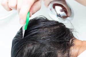 Trained tech using a fine-tooth metal lice comb to work through a section of wet, conditioned hair near the scalp during a professional lice removal session.