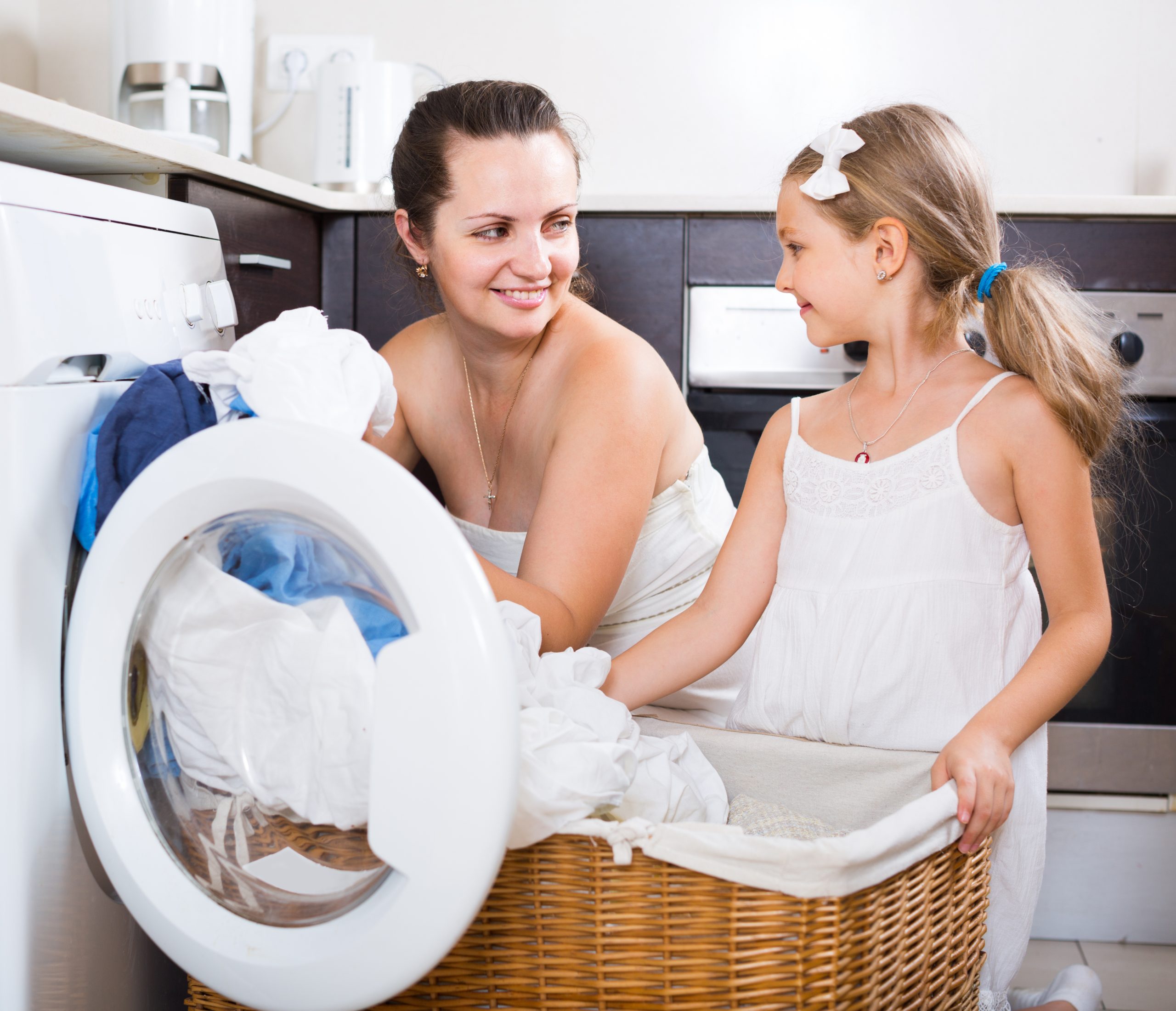housewife and her daughter with linen near washing machine
