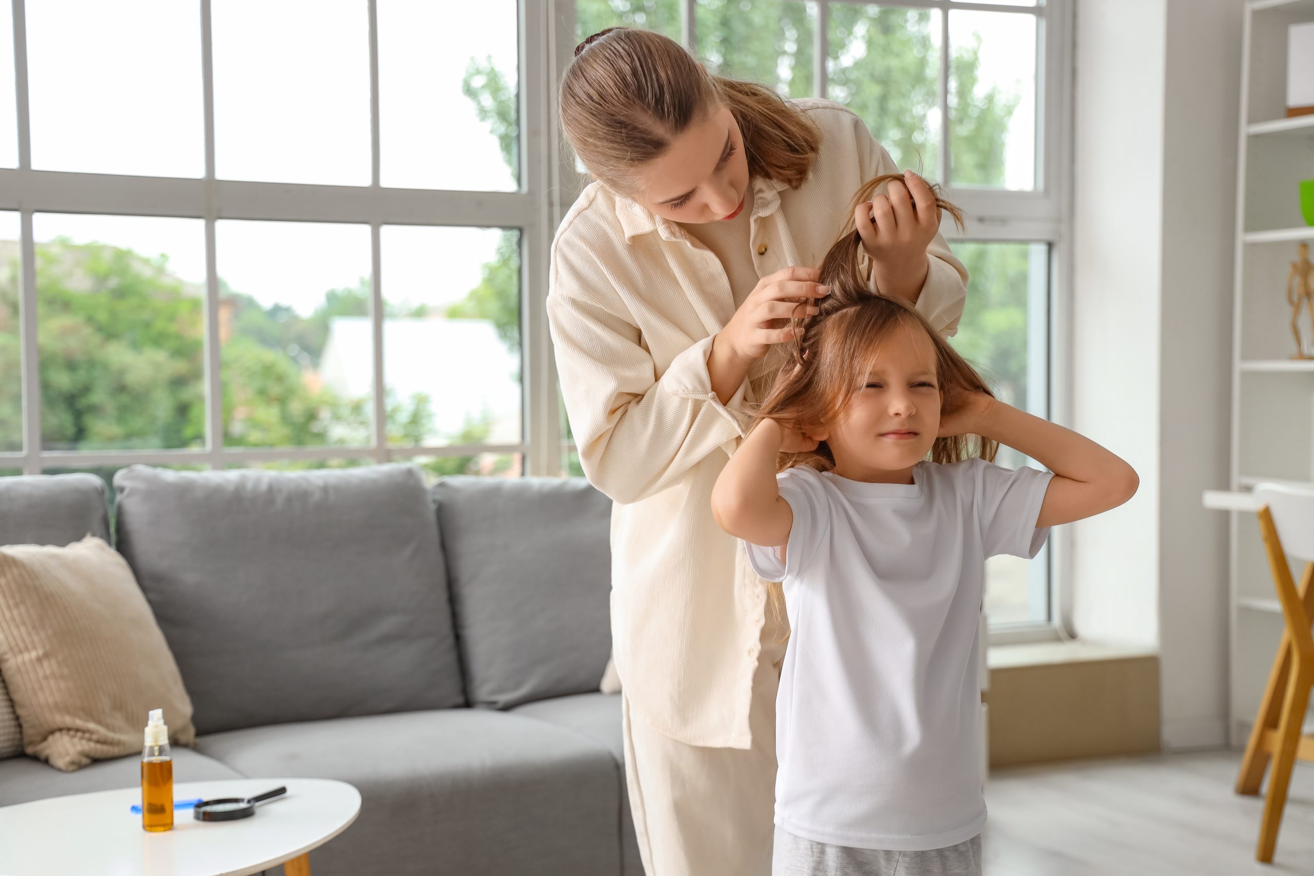 An Omaha mother parts her young daughter's hair under good light to check the scalp for nits and live lice at home, the exact moment a parent tries to tell whether lice eggs with no visible bugs mean an active case.