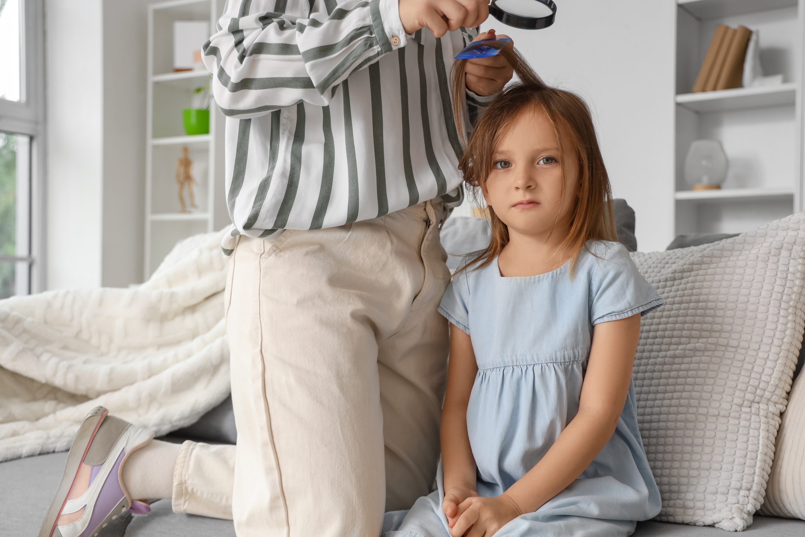 Parent checking a child's hair with a comb and magnifying glass at home.