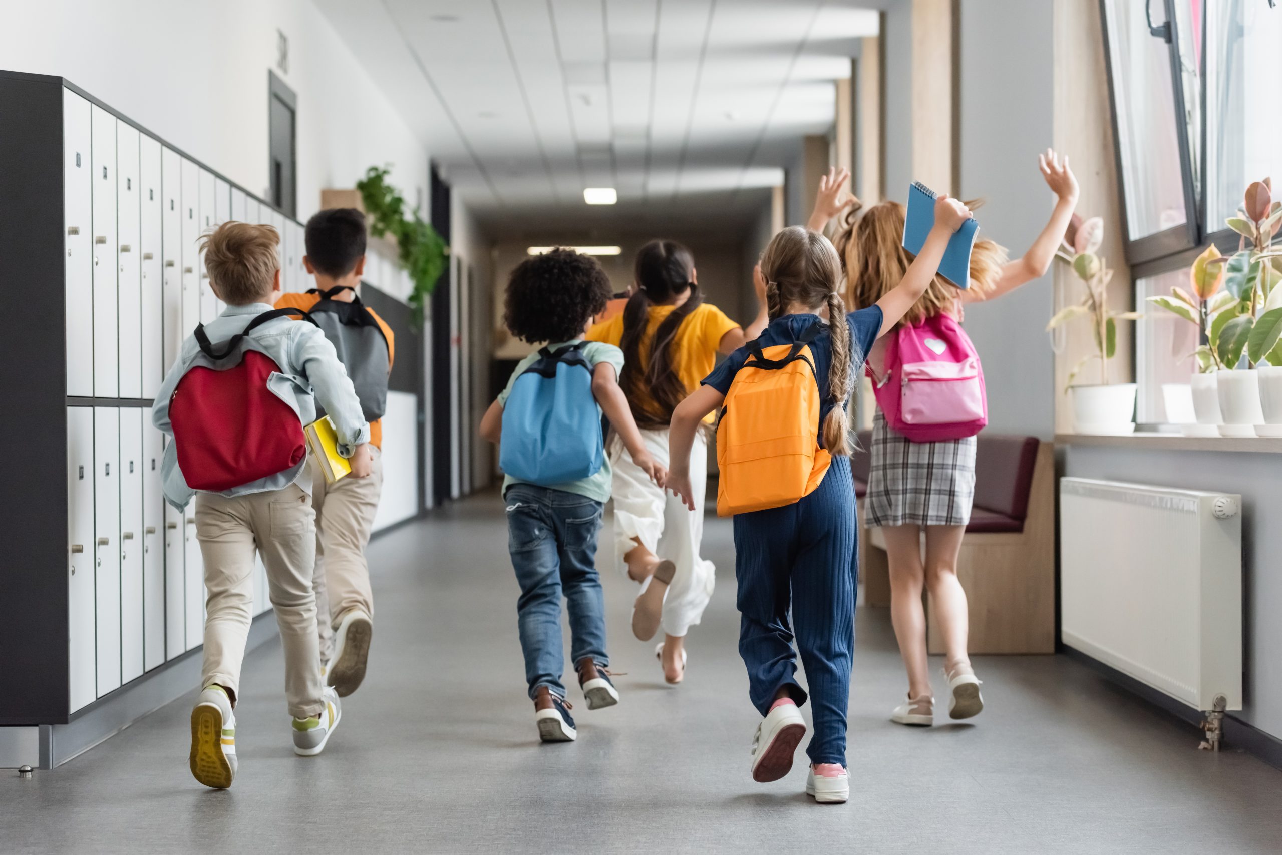 Elementary students walking through a school hallway with backpacks.