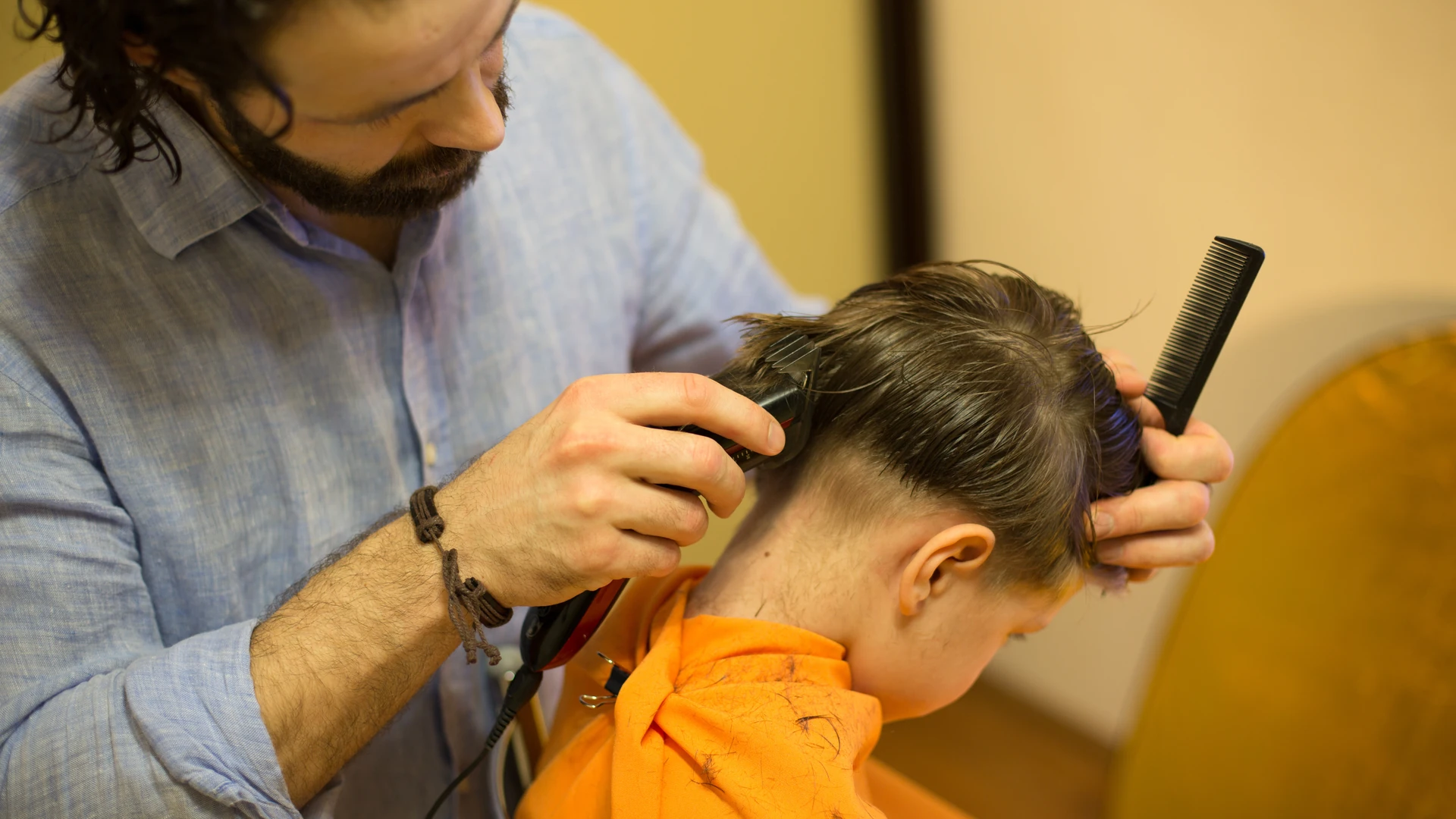 A man gives a boy a clipper haircut at a salon.