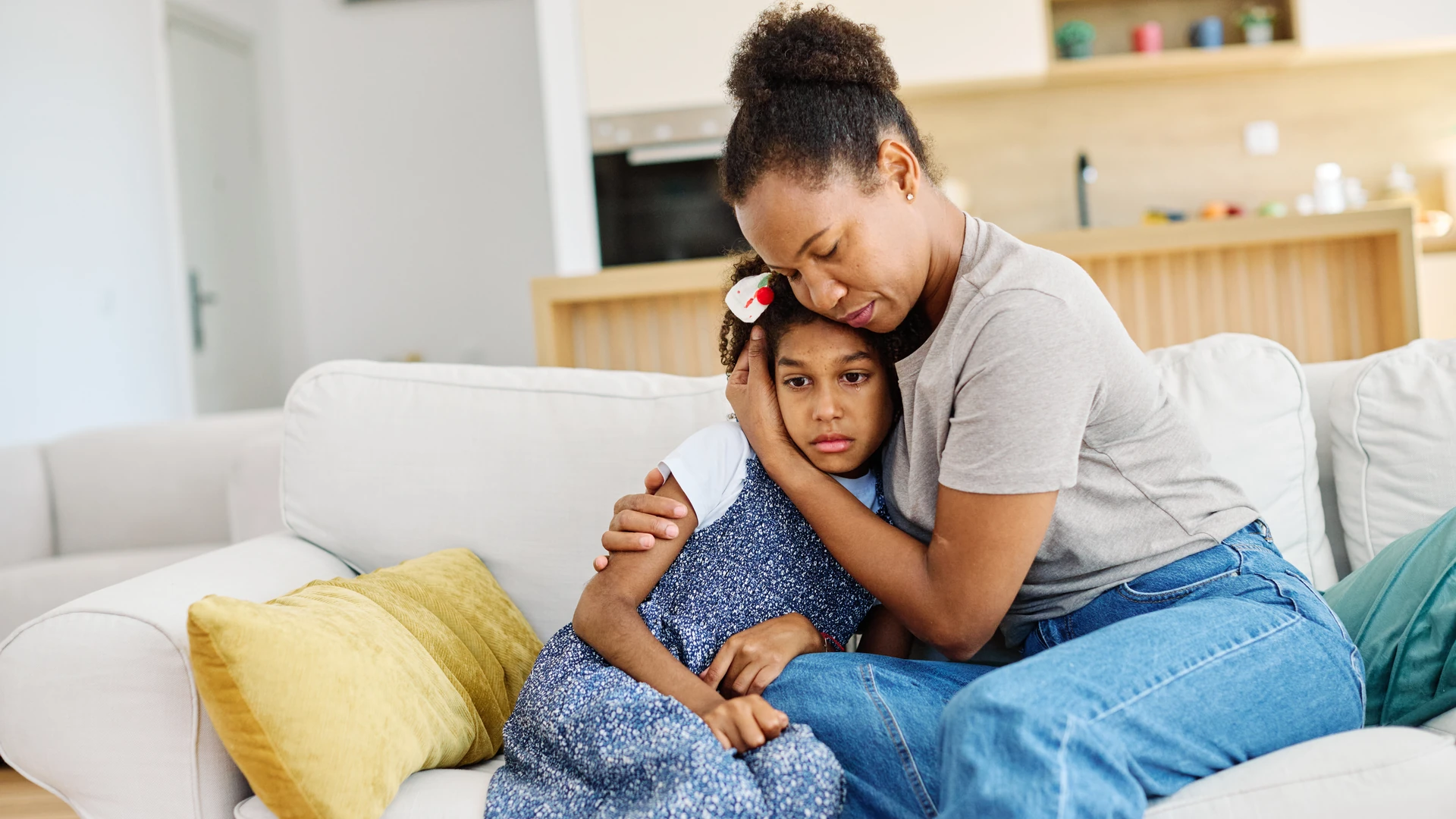A mother embraces her daughter while sitting on a couch.
