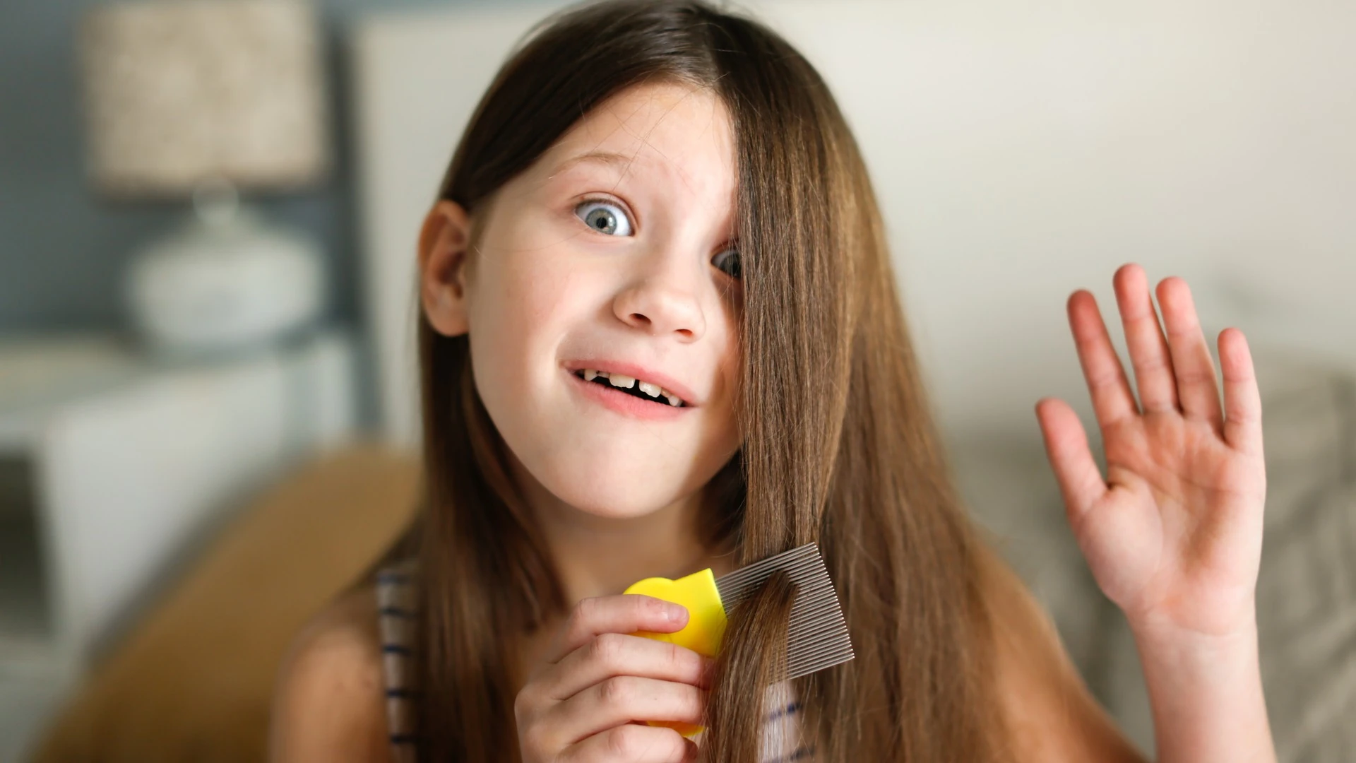 A girl holds a lice comb near her hair with a surprised, playful expression.