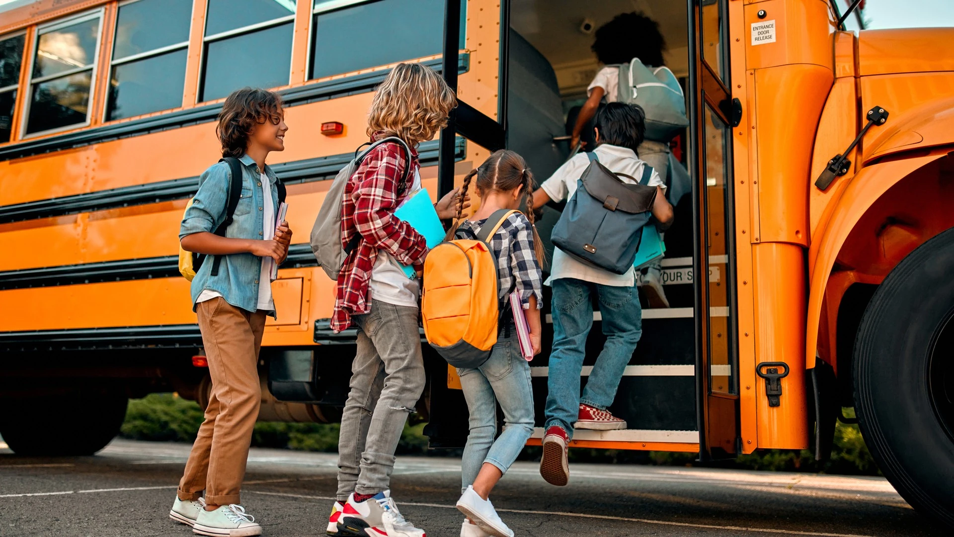 Children with backpacks board a yellow school bus.
