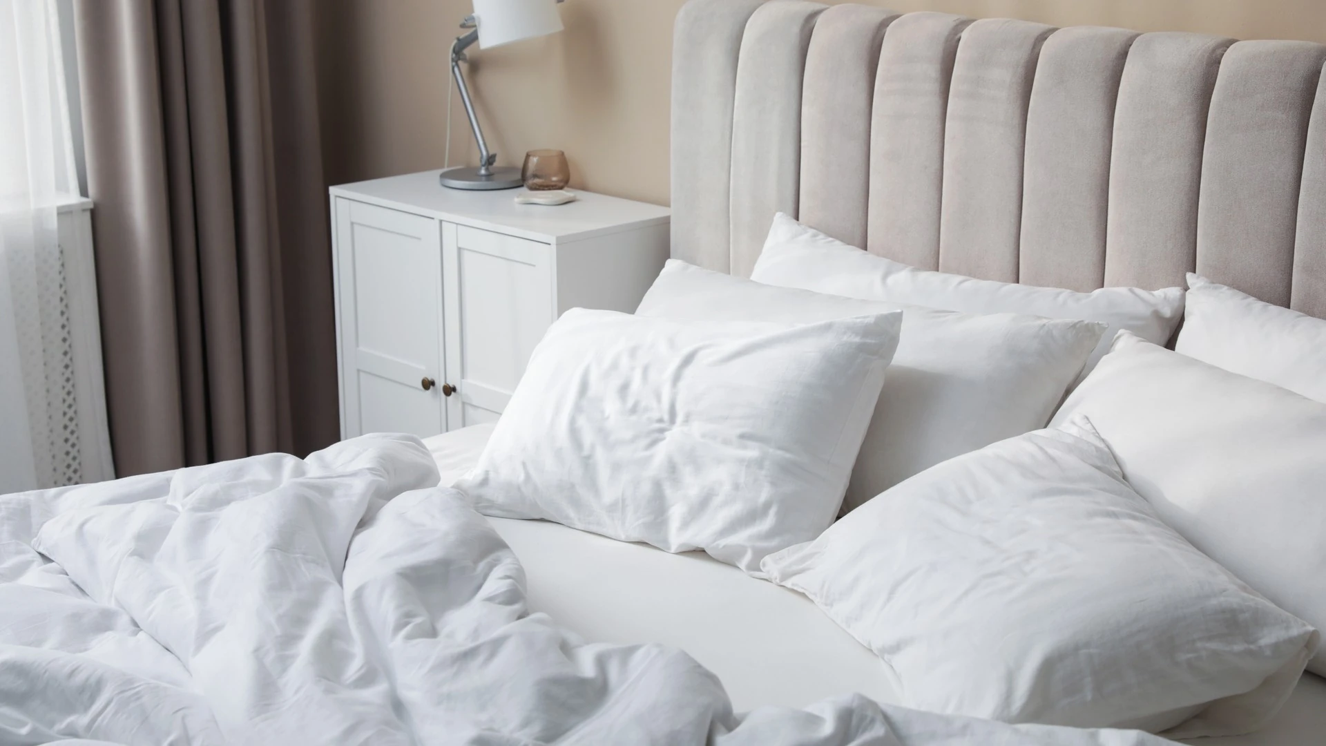 White pillows and a rumpled duvet on a bed in a bedroom.