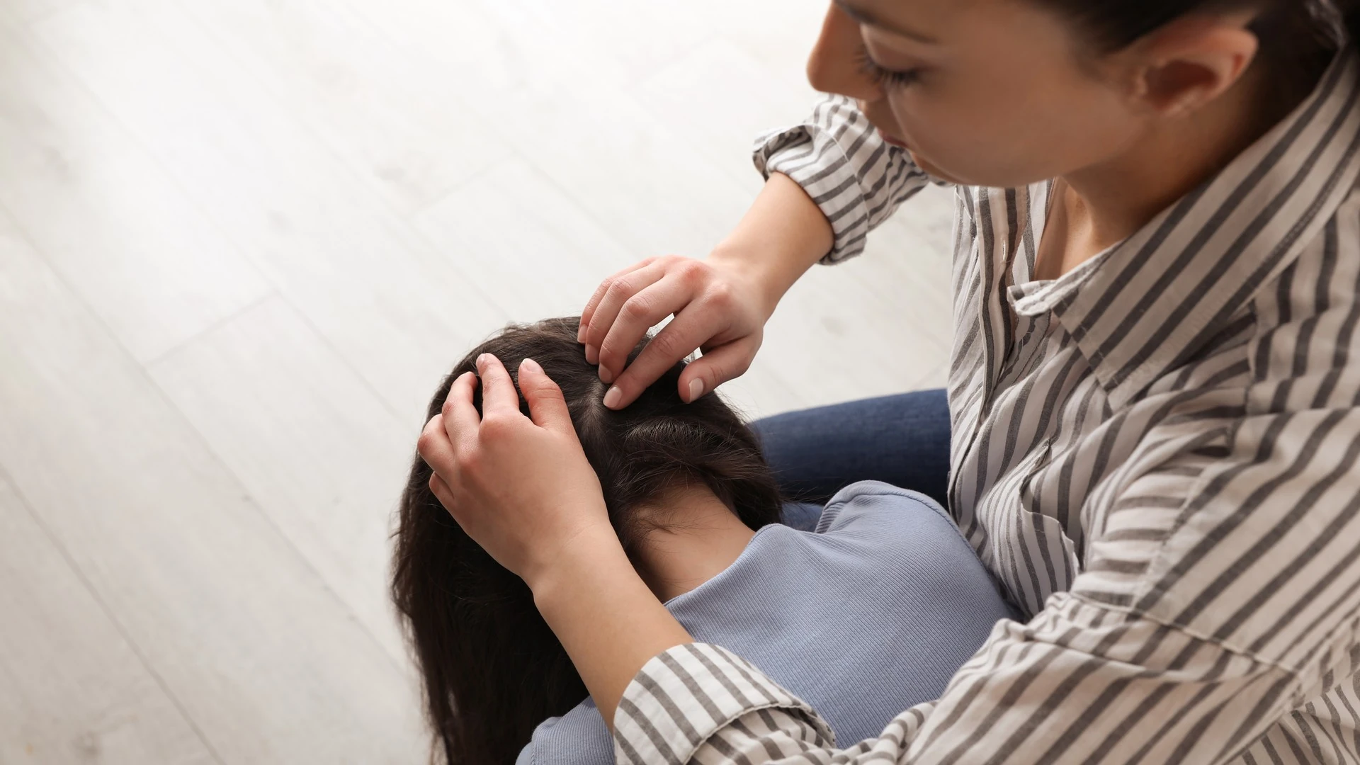 A mother examines her daughter's scalp and hair indoors.