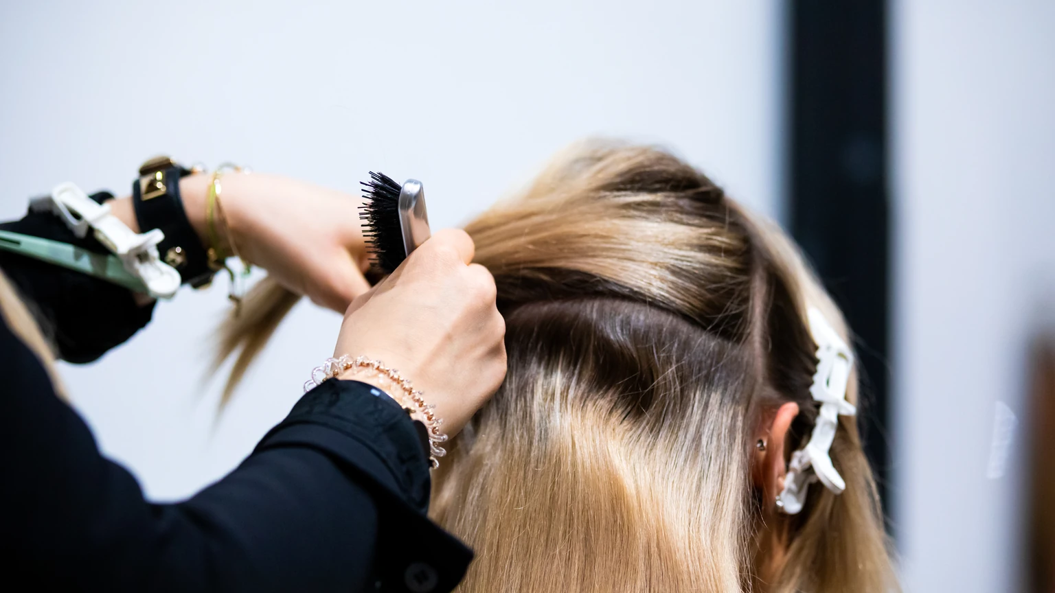 Stylist sectioning long blonde hair at the roots with a brush and clips during an extension appointment