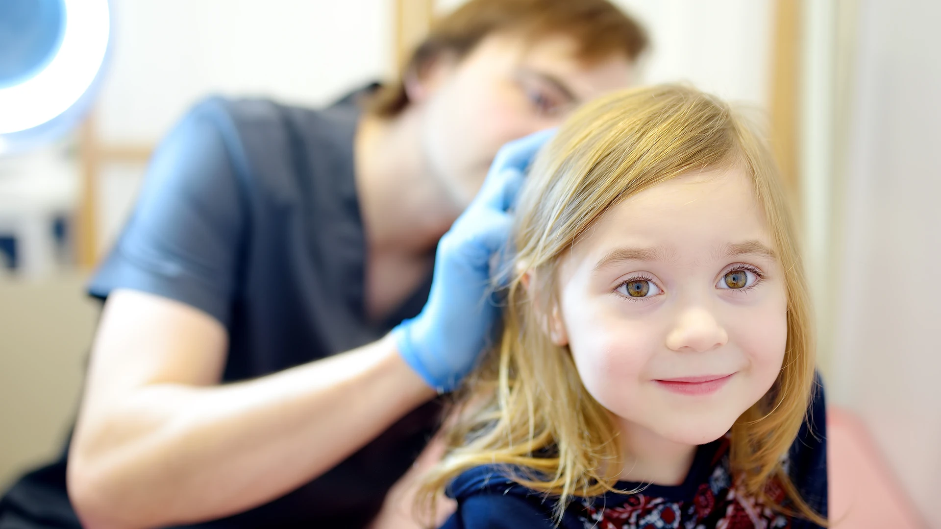 Gloved hands check a smiling girl's hair and scalp.